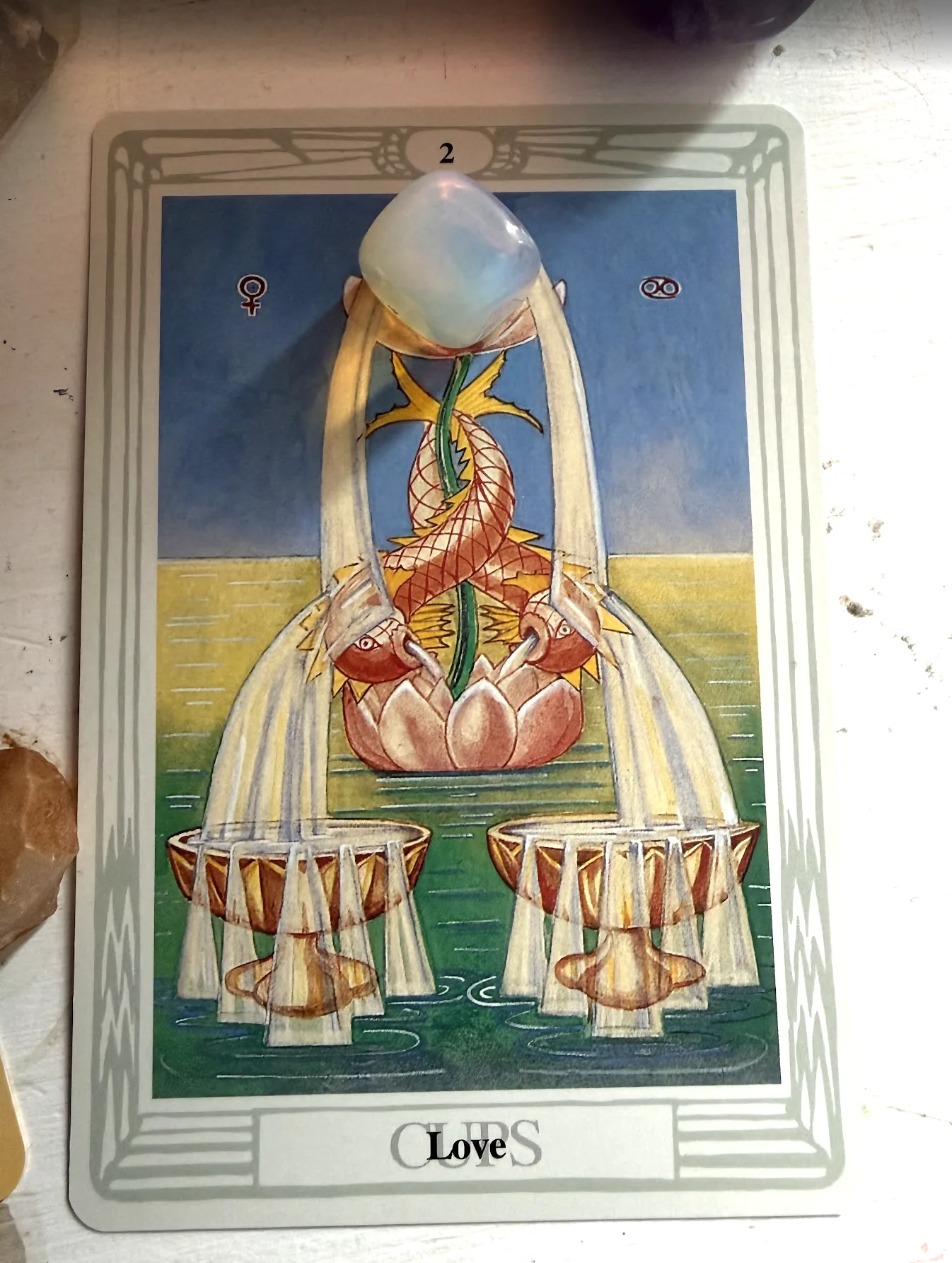 Thoth Tarot Two of Cups Love card with two fish, lotus blossoms, flowing water, golden cups, and a pale crystal