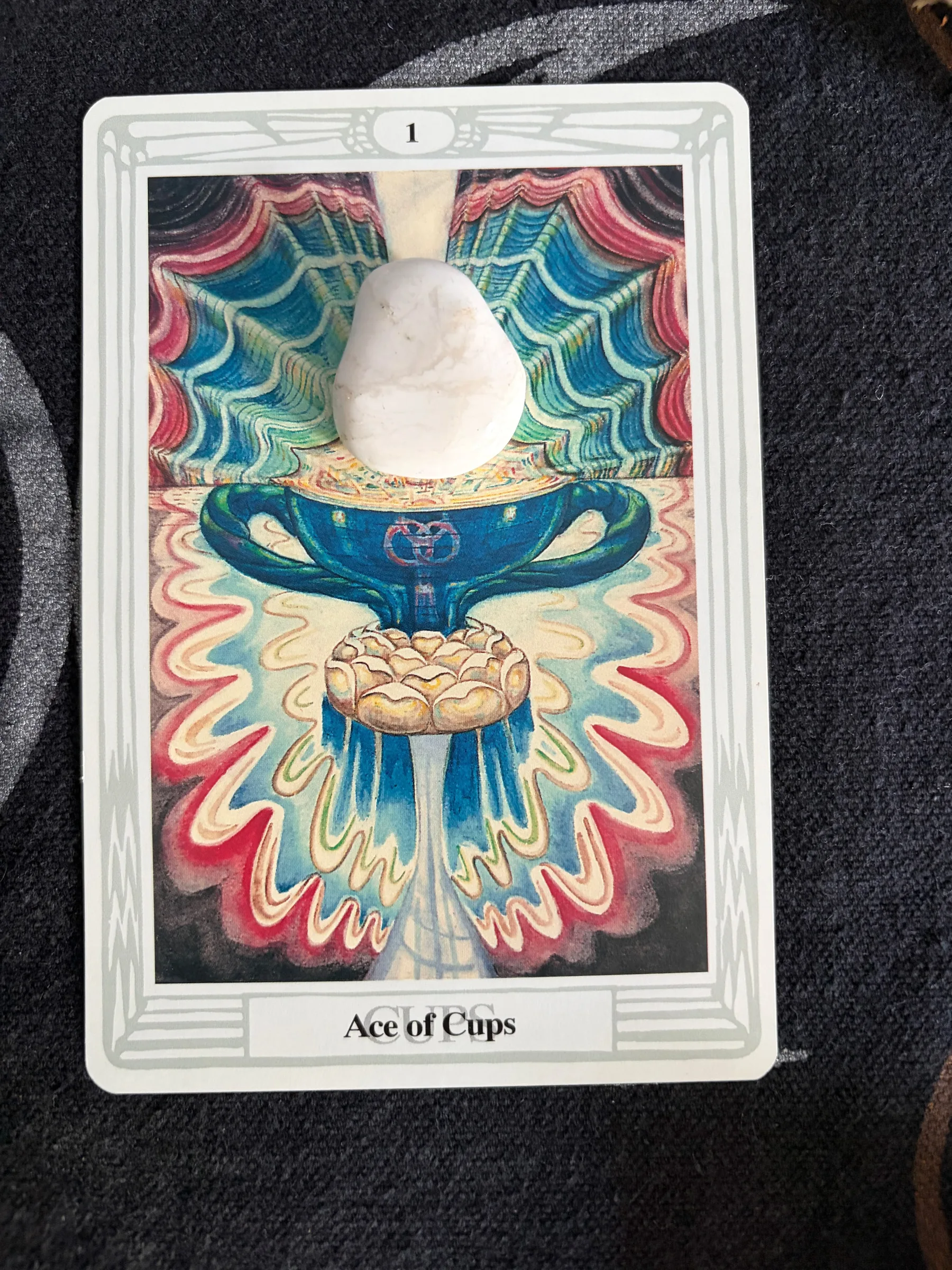 A blue cup with a white stone, surrounded by colorful, swirling patterns, representing the Ace of Cups.